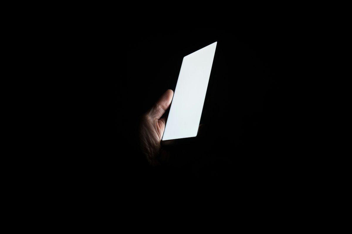 暗い部屋で、明るく光るスマートフォンを持つ手元