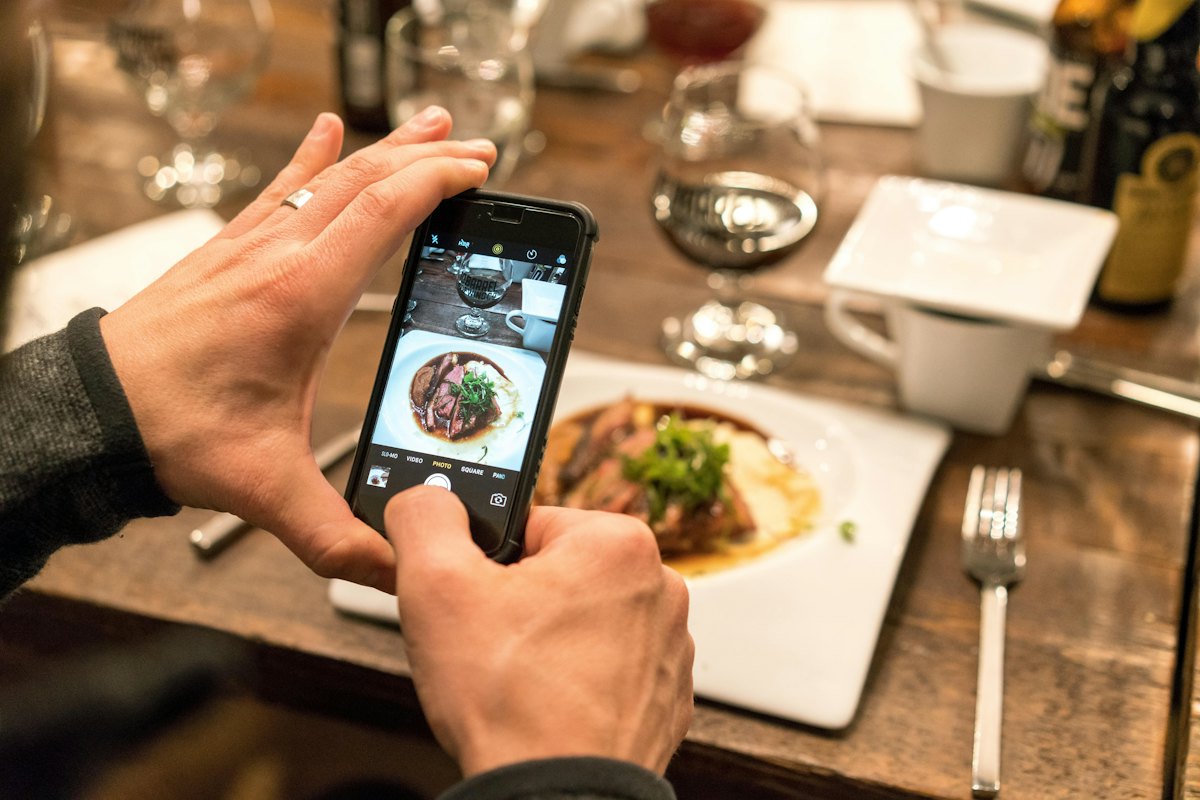 テーブルの料理をスマートフォンで撮影している手元